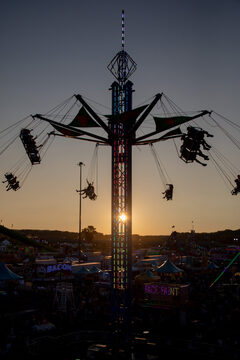 Fairgoers fly high about the crowds on the ground on the three-person swing ride featured in the Midway. As the sunsets and shadows get long, parents holding tired children or large stuffed animals won at games start to make their way to the exit. 
