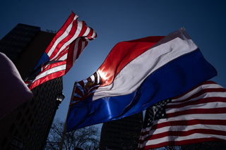 Two American flags and two Karen flags are held high at the front of the demonstration.